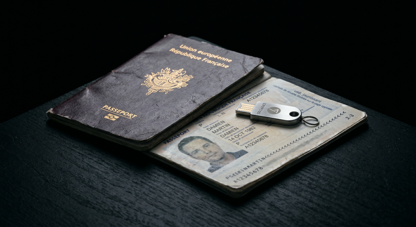 Photographie macro d'un passeport officiel usé et sombre posé à côté d'une clé USB cryptographique en métal argenté sur un bureau noir.